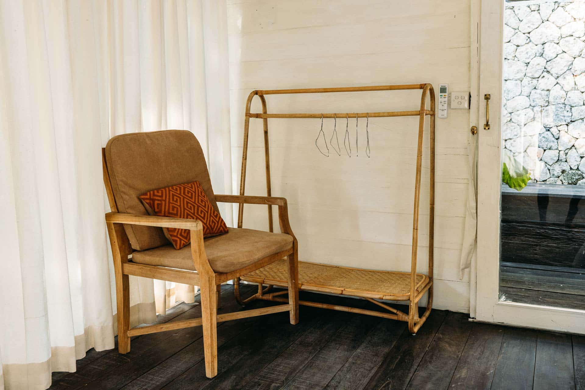 A beige armchair with a clothes rack inside a Balinese hotel room