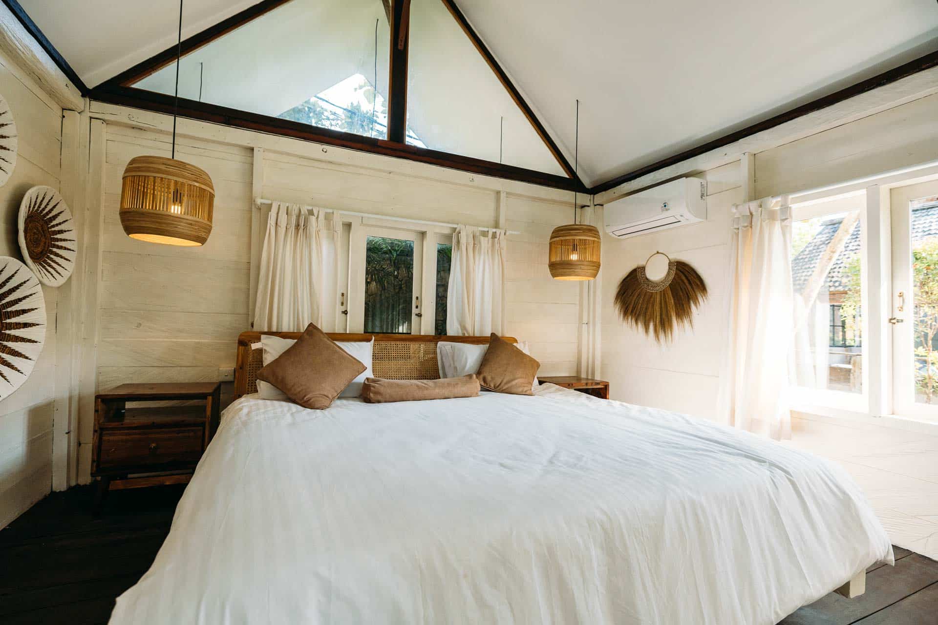 a balinese hotel room decorated in earth tones and white with wide window and garden view