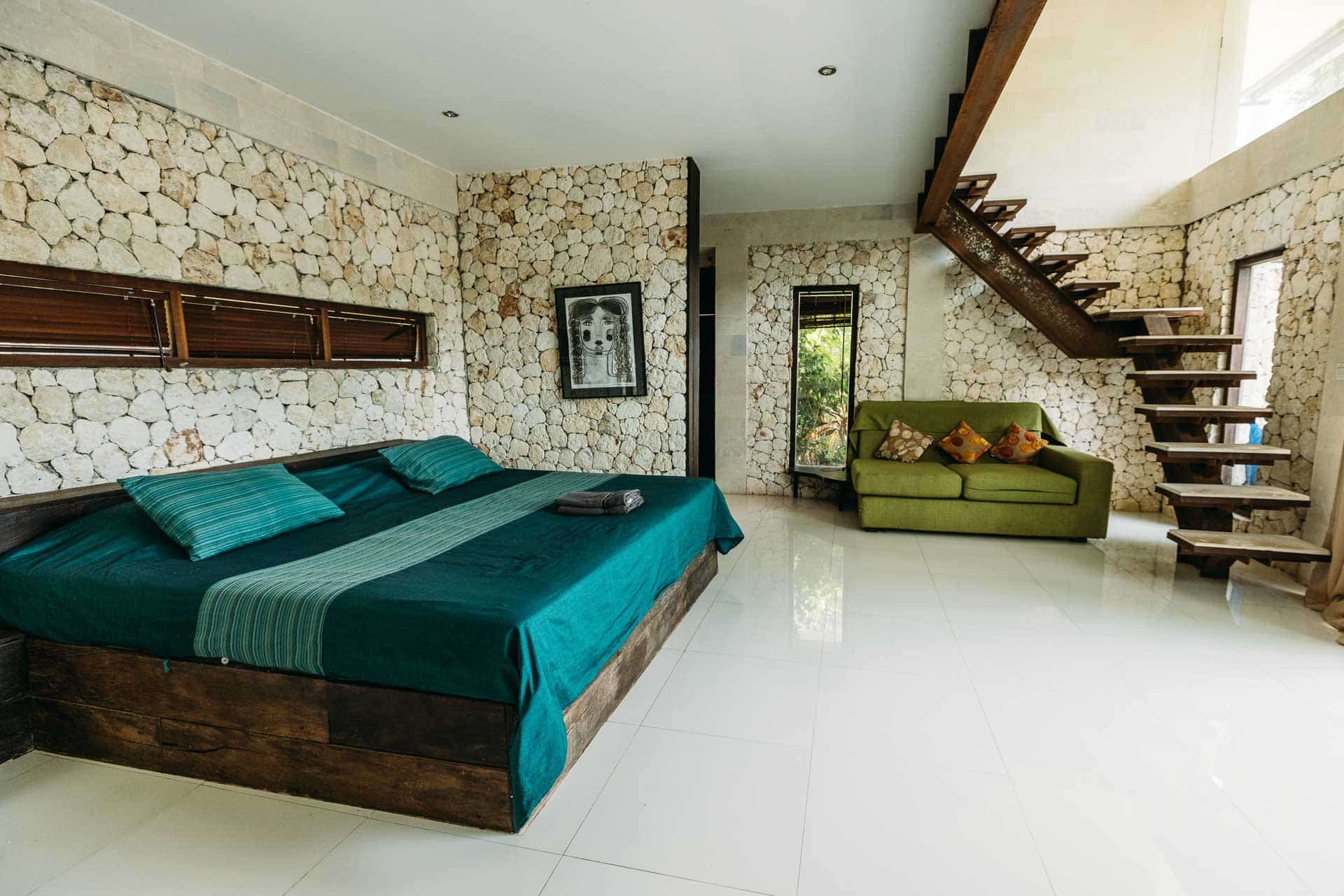 A room in hotel with stones for walls and green sofa and a king-size bed decorated in a rustic way