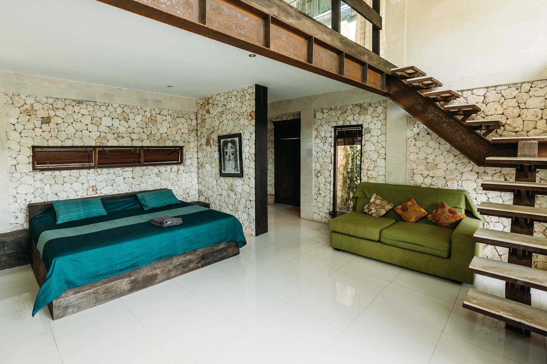 A room in hotel with stones for walls and green sofa and a king-size bed decorated in a rustic way