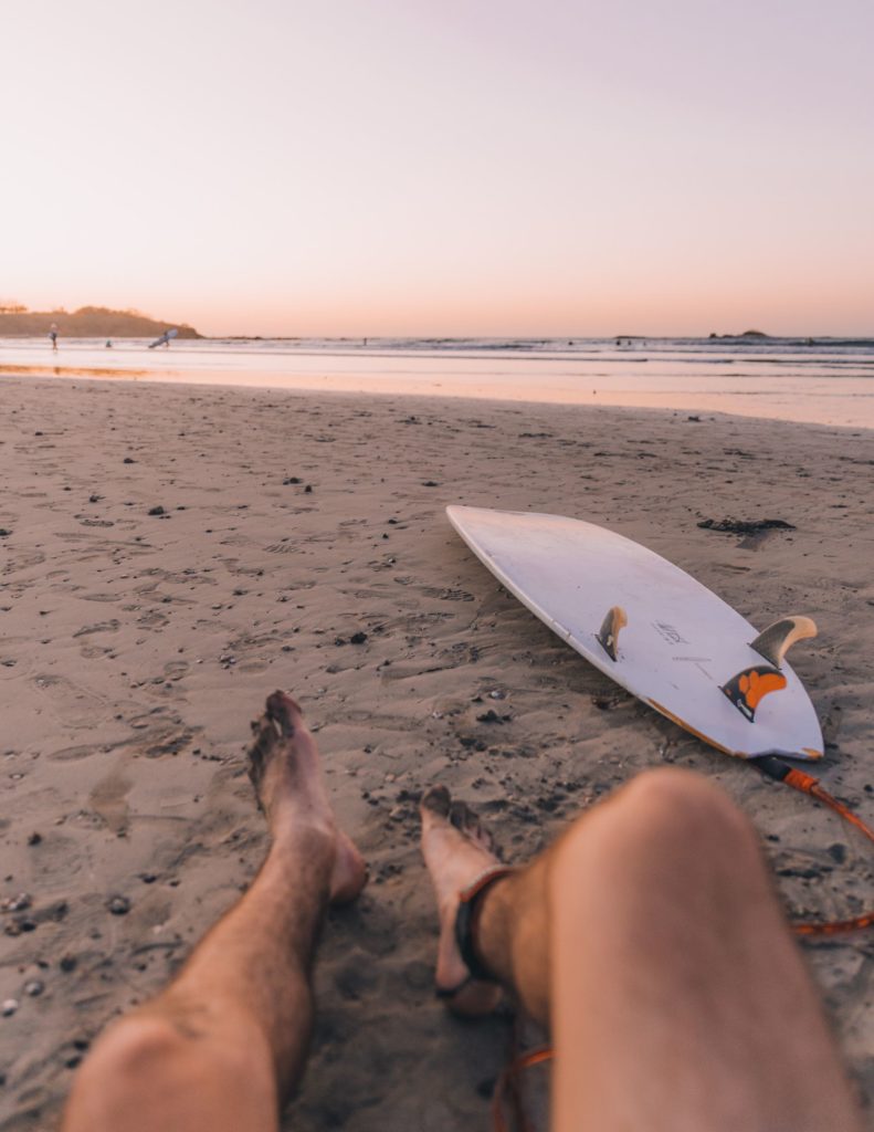 Mann sitzt am Strand in Costa Rica mit Surfbrett