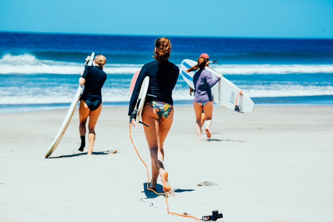 Three surfer girls heading to sea with waves