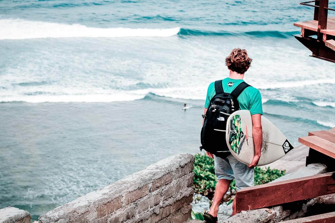 Picture of a surfer walking with his board towards Uluwatu