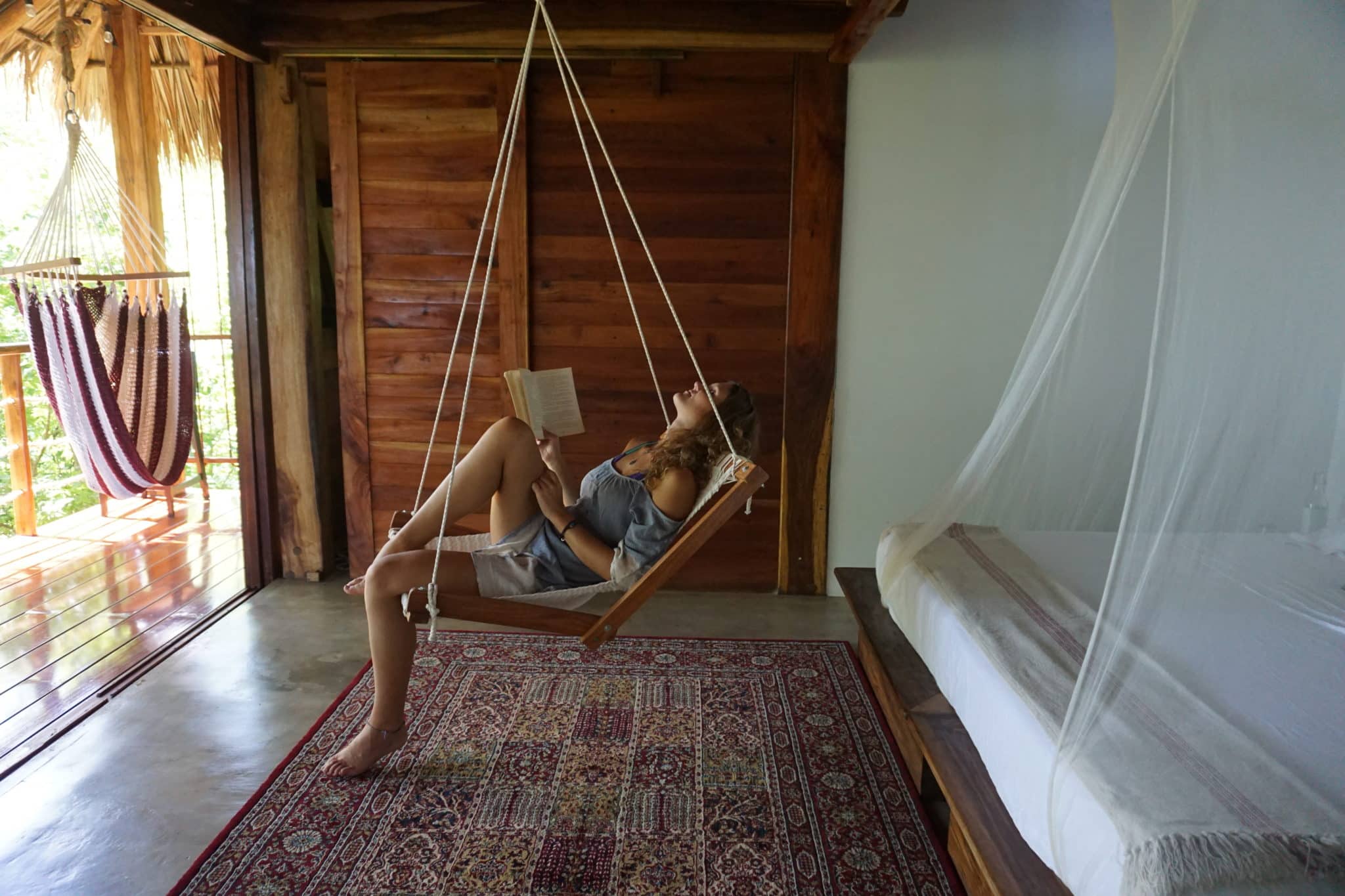 woman reading a book sitting in a hammock chair in room