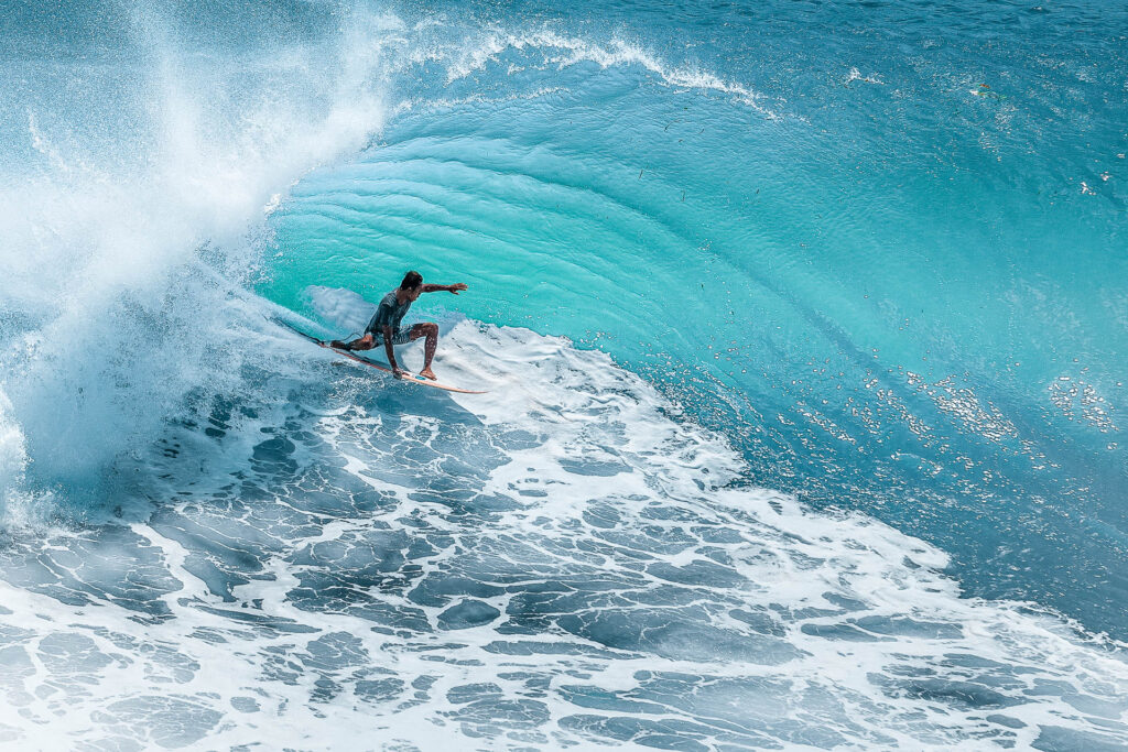 A person on a surf board on a giant wave in blue waters