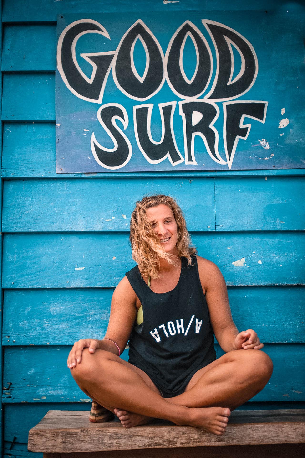 A person sitting crossed legged under a sign that says 'Good Surf'