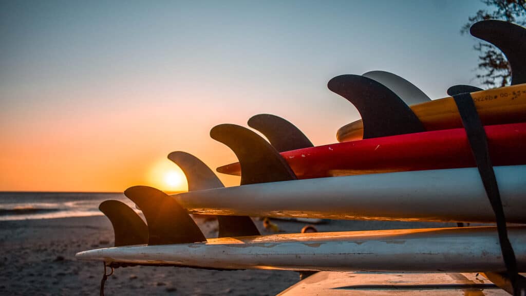 A picture of surfboards stacked on top of each other with the sunset in background.