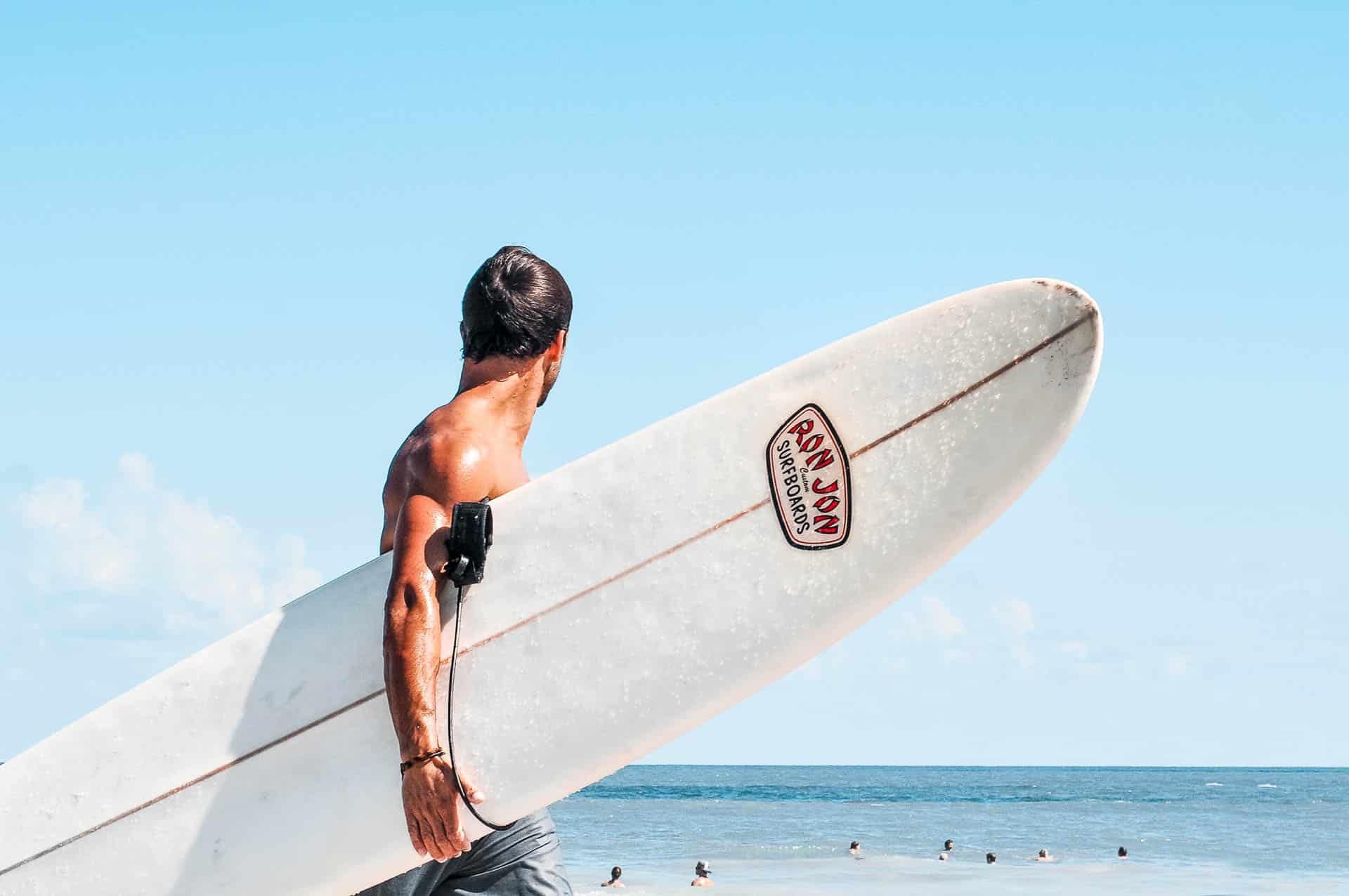 A man carrying a white surf board and looking into the ocean