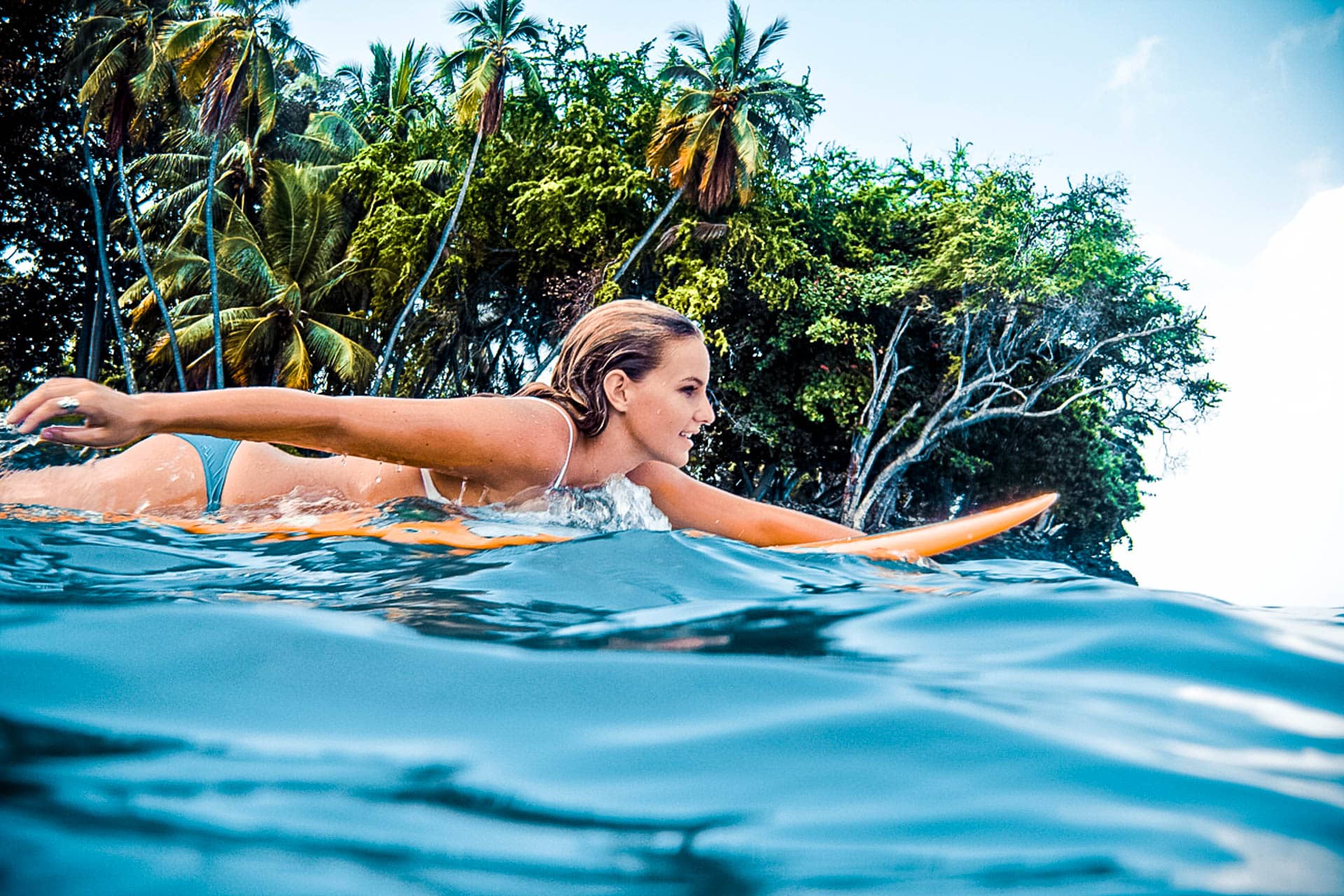 A person in bikini paddling on an orange surf board