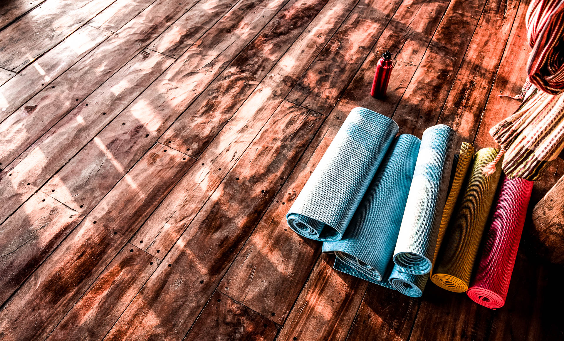 Wooden floor with multiple yoga mats rolled up and kept together.
