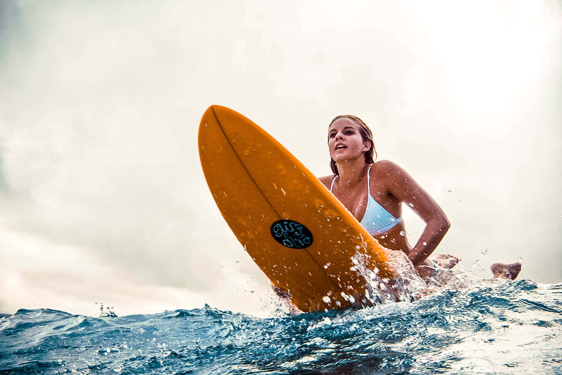 A girl in white bikini on a yellow surfboard in the ocean