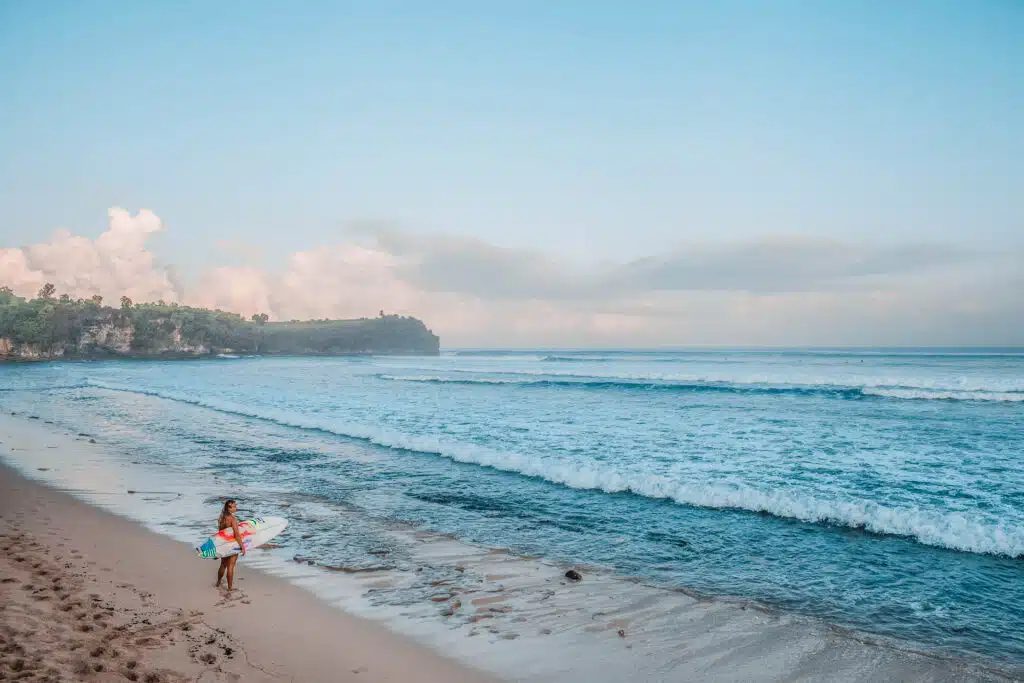 A person standing with the surfboard looking at the waves