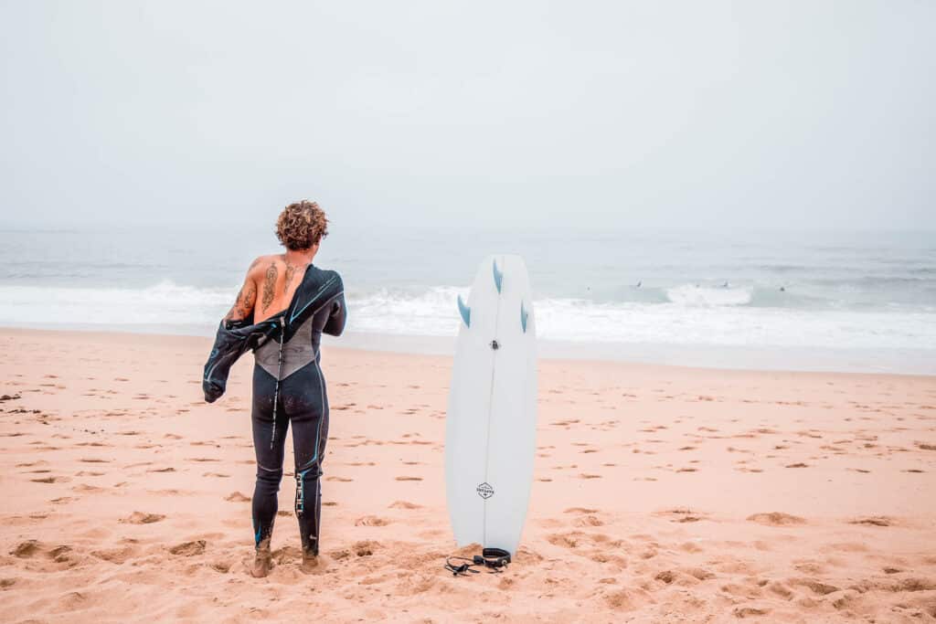 Person with tattoed back removing a wetsuit looking at the ocean.