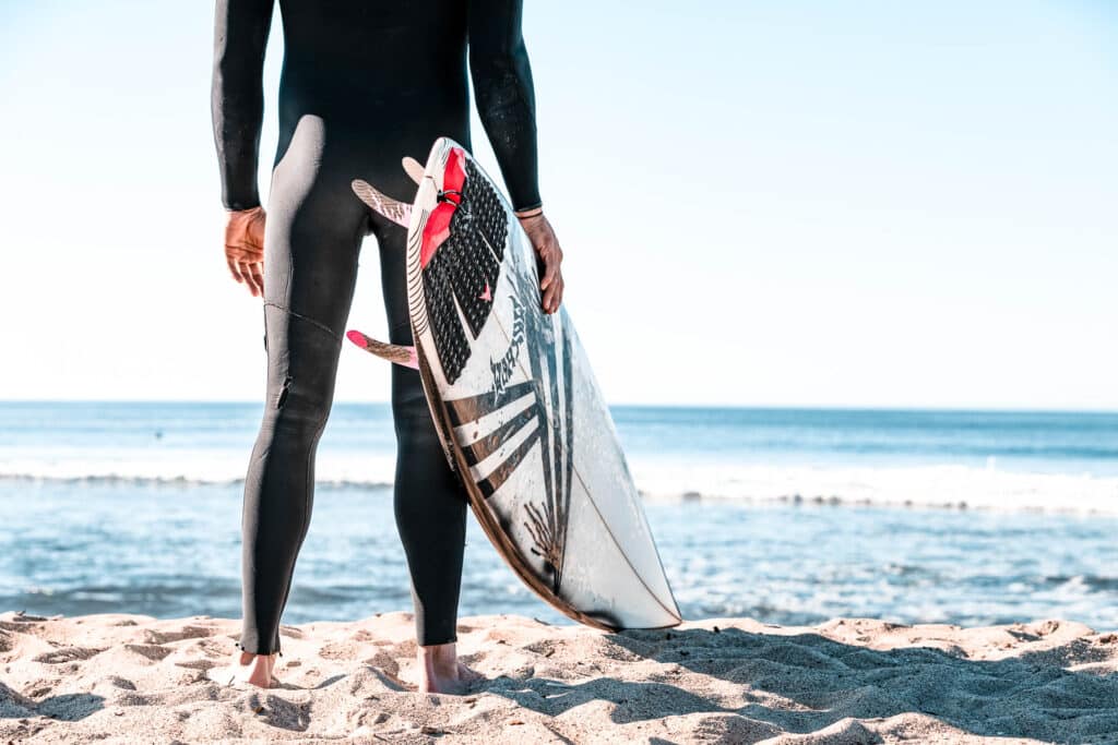 A person standing at the beach with surfboard in hand while looking at the beach.