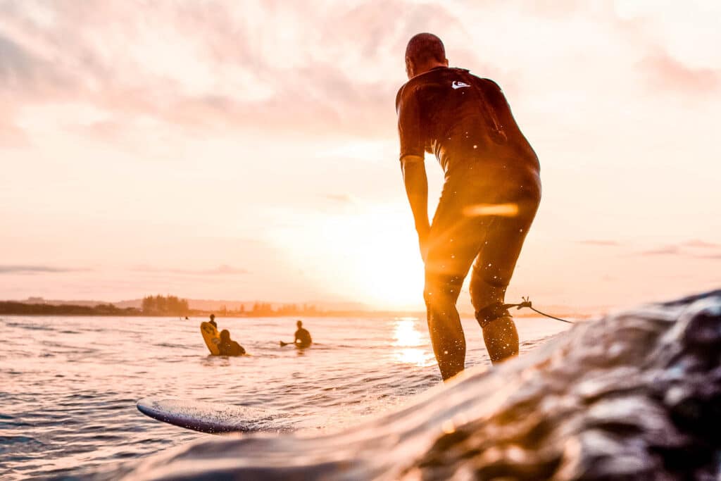 A person standing on surfboard looking towards the sunset.